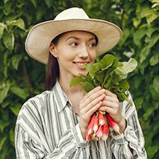 Young woman harvesting fresh radishes. Lady in a hat. Girl in a garden.
