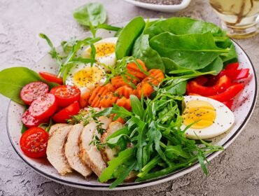 Plate with a keto diet food. Cherry tomatoes, chicken breast, eggs, carrot, salad with arugula  and spinach. Keto lunch