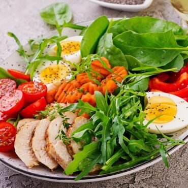 Plate with a keto diet food. Cherry tomatoes, chicken breast, eggs, carrot, salad with arugula  and spinach. Keto lunch